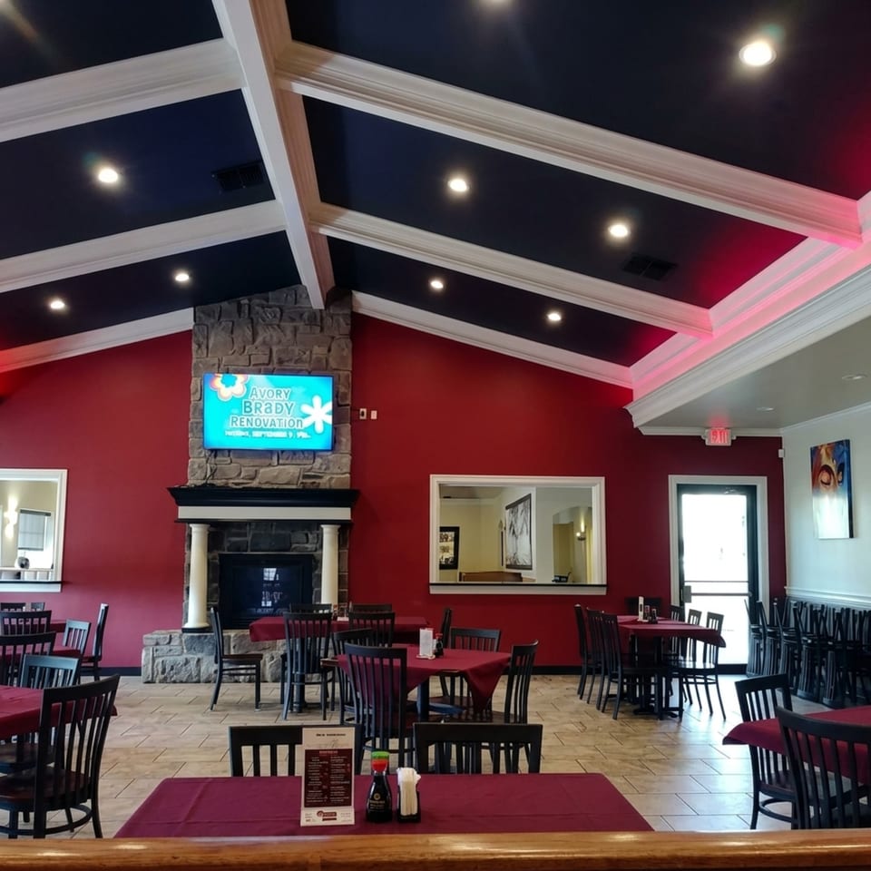 Restaurant interior with red walls, dark tables, and a stone fireplace with a TV screen.