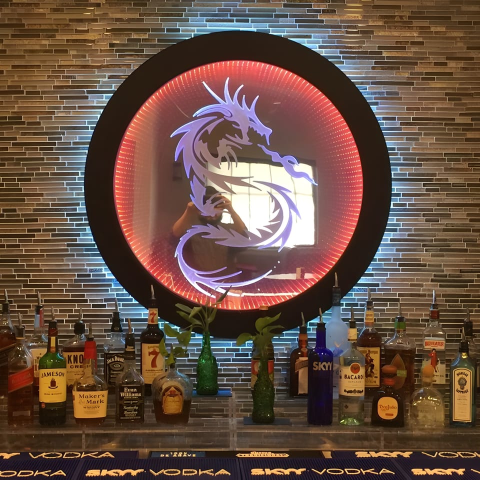 A bar with various liquor bottles and a circular, illuminated dragon logo on a tiled wall.