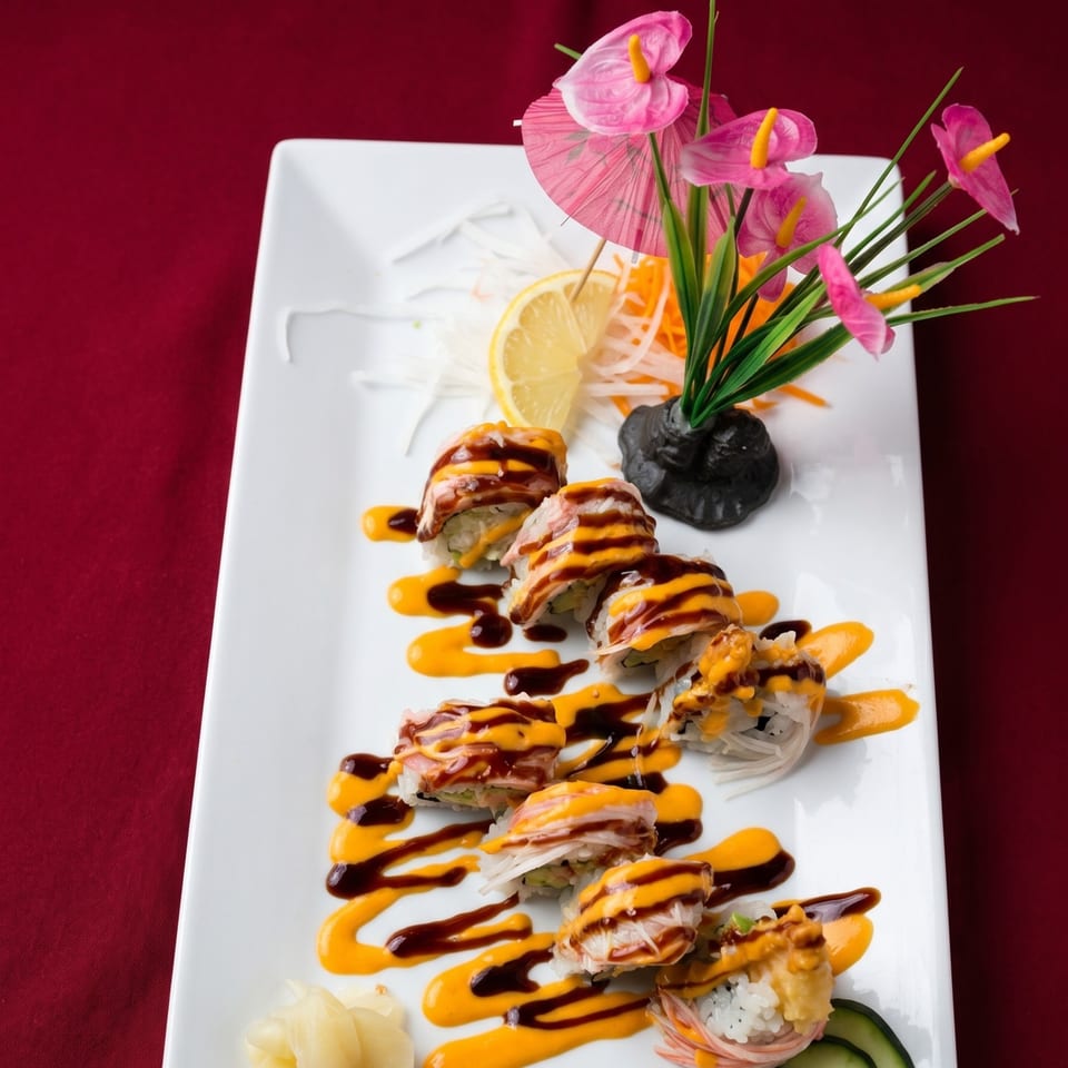 Sushi rolls with orange and brown sauce, garnished with lemon, radish, and pink flowers.