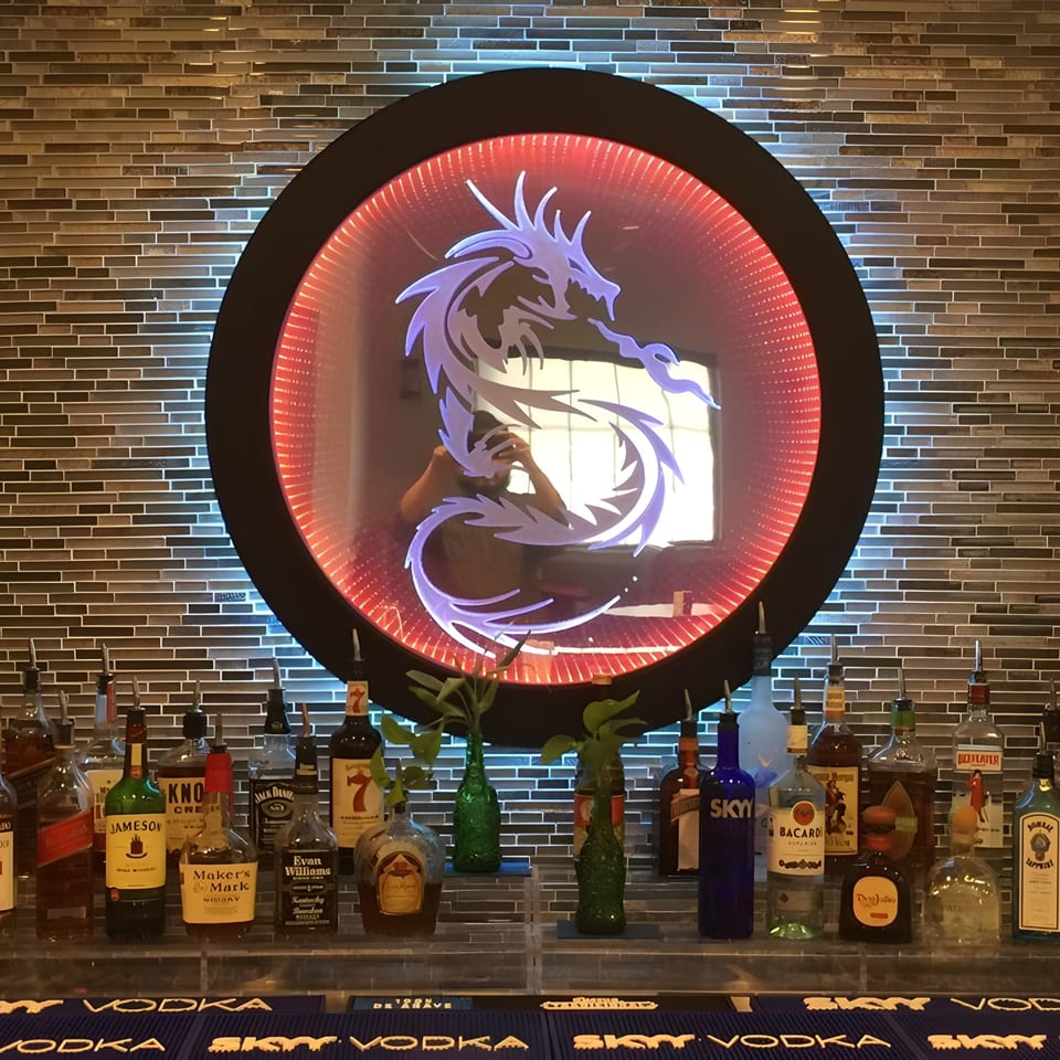 A bar with various liquor bottles and a large circular mirror featuring a glowing purple dragon.