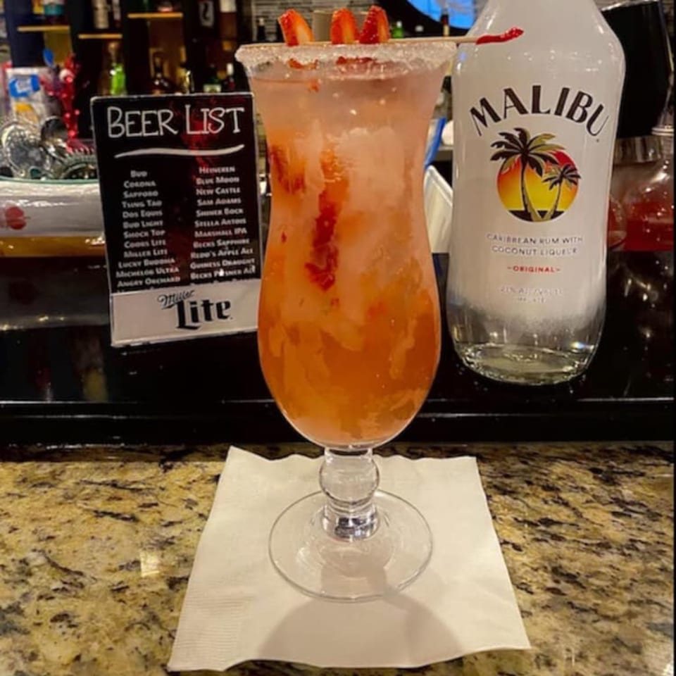 A strawberry cocktail with a sugar rim and strawberry garnish sits on a bar next to a Malibu bottle.
